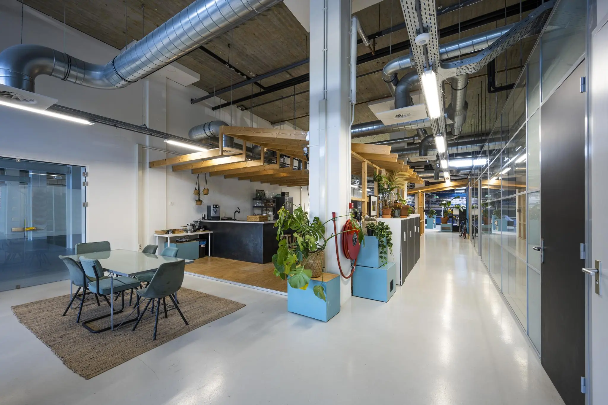 Moderne kantoorruimte aan de Joan Muyskenweg met open keuken, zithoek en industriële plafondleidingen.